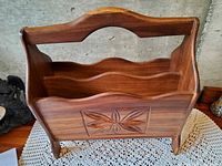 Front three-quarter view of teak magazine rack showing carved floral panel and overall form