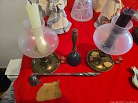 Wide view of both brass chambersticks, hand bell, twisted poker on red cloth