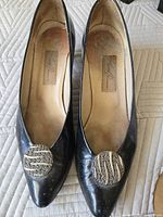 Top view of both pumps showing pointed toes, black patent finish, and decorative metal ornaments