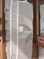 Folded beige and white geometric striped runner rug displayed on furniture surface