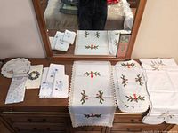 Assorted holiday linens laid out on dresser: runner, doilies, napkins/towels
