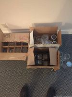 Two divided cardboard boxes containing over two dozen small clear glass jars, some with metal lids visible