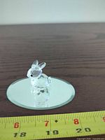 small faceted crystal bunny on round mirror base with measuring tape showing scale