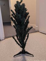 Full view of the green artificial tabletop Christmas tree on its black plastic stand
