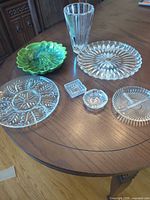 Seven items displayed on table: three round pressed glass plates, one fluted vase, one green ceramic bowl, two small pressed glass dishes