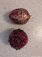 Egg-shaped red glass ornament and berry-covered ball ornament on tabletop
