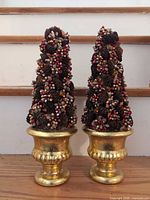 Pair of cone-shaped pine cone arrangements with red and gold berry accents on gold urn bases
