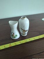 Two small white porcelain bud vases beside ruler showing <4 in height; motifs of bird on branch and lighthouse scene visible
