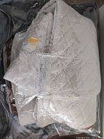 Diamond-quilted beige polyester table pad folded in clear storage bag
