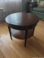 Front perspective of round dark brown wood end table showing top surface and lower shelf
