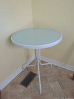 Full view of round white metal side table with frosted glass top against wall