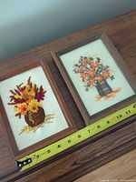 Both framed embroidered pieces beside measuring tape showing 5x7 in size