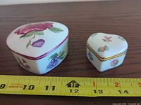 Top view of both heart-shaped porcelain trinket boxes next to ruler for scale