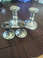 Two medium and two small silver-plated candlestick holders on tabletop