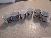 All six ceramic Christmas mugs lined in a row showing graphics and handles