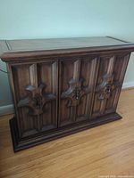 Front view of solid wood walnut sideboard showing three carved doors and brass hardware
