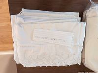 Folded white cotton sheet showing scalloped eyelet embroidery and accompanying note referencing pillowcases
