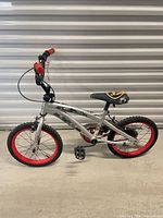 Full left side view of children’s silver bicycle with red rims and handlebar grips