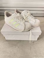 Pair of Adidas children’s Superstar sneakers on box showing side stripes and shell toes