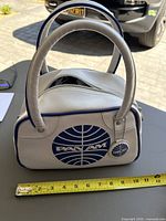 Front view of handbag showing logo, handles, tag, tape measure for scale