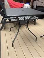 Full view of black metal mesh square patio table on deck