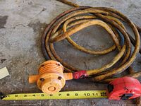 Coiled yellow hose with attached orange inline pump alongside measuring tape