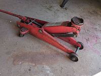 Side view of red steel hydraulic floor jack with handle and saddle pad
