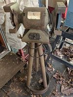 Full view of 6 in. bench grinder mounted on rusted steel tripod pedestal, showing right grinding wheel and left wire brush