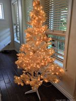 Assembled white/ivory pre-lit tree on plastic stand, lights illuminated
