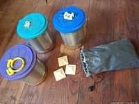 Three tins with coloured lids, four adhesive bases and drawstring pouch on floor