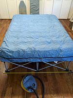 Full view of blue air mattress on folding frame with foot pump in foreground