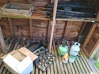 Overall view of lot inside shed: wooden sifter, rolled plastic mesh with stakes, toolbox with fittings, box with burlap, sprayers on floor
