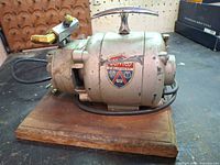 Full left-front view of Gomco pump on wood base showing decal and outlet fitting