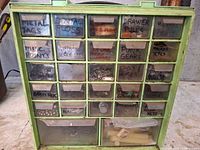 Front view of organizer showing green cabinet and labelled clear drawers with contents