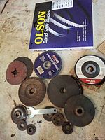 Lot overview showing Olson bandsaw blade package, assorted grinding and cutoff discs, flanges and wrench