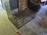 Full view of black wire dog crate with door open, tape measure alongside