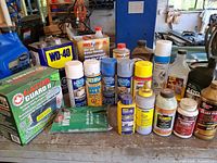 Overall lot on workbench showing multiple aerosols, solvents, oils, epoxy kit