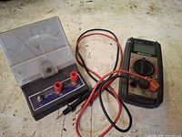 Digital multimeter, analog voltmeter, test leads on workbench