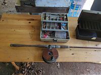 Tabletop view showing fishing rod with reel, beige tackle box with contents, black tackle box closed
