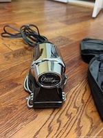 Front view of Oster chrome/black handheld percussion massager with power cord visible