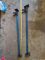 Full view of both blue support poles on floor with tape measure for scale