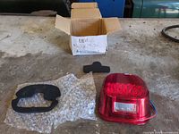 Tail light with lens, wiring, two foam gaskets and box displayed on workbench