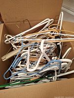 Open box filled with a variety of plastic, wood, and metal hangers