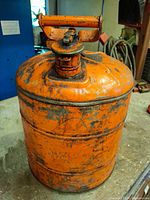 Full front view of orange steel fuel can showing body and spout