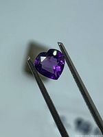 Heart-shaped purple amethyst held in tweezers, showing faceted crown