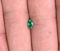 Oval faceted emerald on fingertip showing size and color