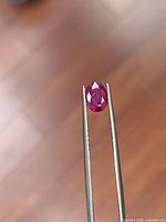 Front view of oval faceted ruby held in tweezers