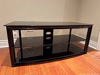 Front view of black glass TV stand showing three shelves and open back