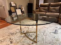 Full view of coffee table in room showing round glass top and gold-tone metal base