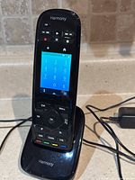 Front view of Logitech Harmony Ultimate One remote seated in charging cradle with power adapter visible
